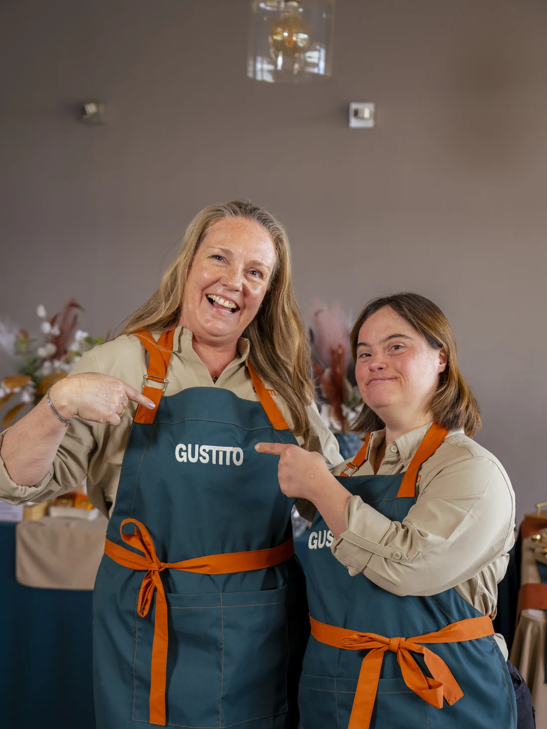 Mónica apunta el logo de Gustito en su delantal y Camila la apunta a ella